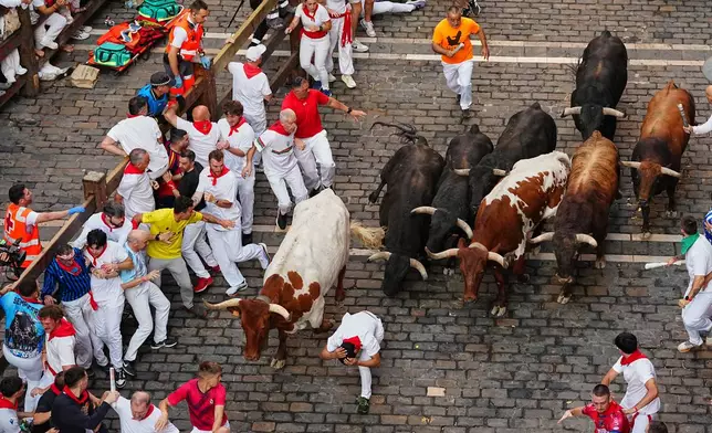 Revelers run alongside Victoriano del Río's fighting bulls during the third running of the bulls at the San Fermín festival in Pamplona, Spain, Thursday, July 9, 2026. (AP Photo/Miguel Oses)