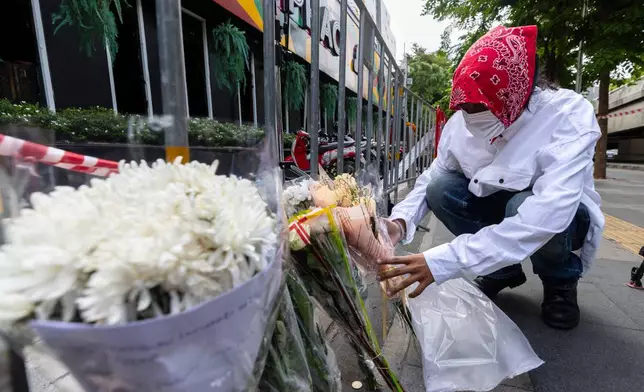 A man puts flowers outside the music bar where a fire killed a number of people in Bangkok, Thailand, Tuesday, July 14, 2026. (AP Photo/Wason Wanichakorn)