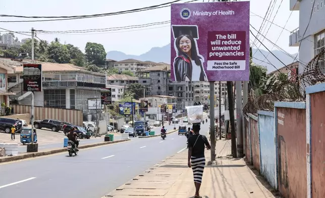FILE - A woman walks past a billboard promoting the Safe Motherhood Bill on Wilkinson Road in Freetown, Sierra Leone, March 12, 2025. (AP Photo/Caitlin Kelly, File)