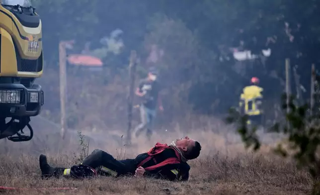 A firefighter lays on the ground after working to extinguish a fire in the forest near Blagon, during wildfires in southwestern France, Wednesday, July 29, 2026. (AP Photo/Emma Da Silva)