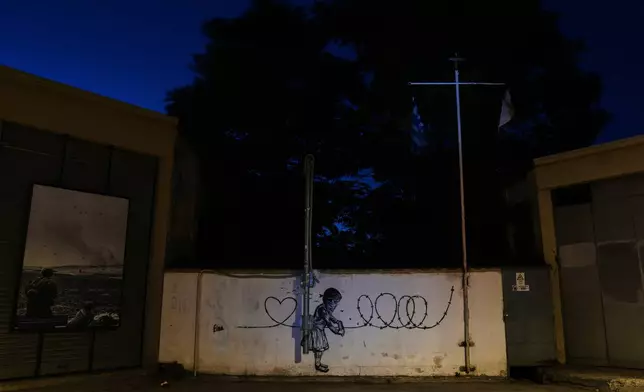 Graffiti depicting a girl painting barbed wire into a heart covers a wall along a blocked road separating the Greek Cypriot south from the Turkish Cypriot north, along the U.N.-controlled buffer zone established after the July 20, 1974 Turkish invasion of Cyprus, in the medieval core of the divided capital, Nicosia, Cyprus, on July 13, 2026. (AP Photo/Petros Karadjias)