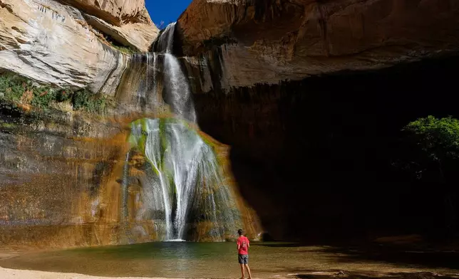 FILE - A hiker watches a waterfall at Lower Calf Creek Falls at Grand Staircase Escalante National Monument, July 12, 2023, in Escalante, Utah. (AP Photo/Ross D. Franklin, File)