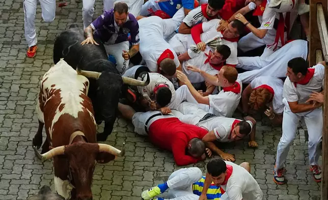 Revelers fall next to Jandilla's fighting bull during the eigth running of the bulls at the San Fermín festival in Pamplona, Spain, Tuesday, July 14, 2026. (AP Photo/Miguel Oses)