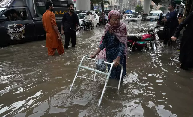 A elderly women wade through a flooded road caused by heavy monsoon rain in Lahore, Pakistan, Wednesday, July. 22, 2026. (AP Photo/K.M. Chaudary)