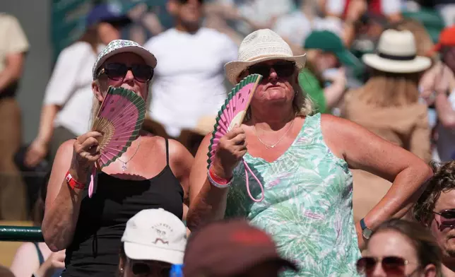 Spectators cool themselves with a hand fan as they watch the second round men's singles match between Alexander Zverev of Germany and Valentin Royer of France, at the Wimbledon Tennis Championships in London, Thursday, July 2, 2026. (AP Photo/Maja Smiejkowska)
