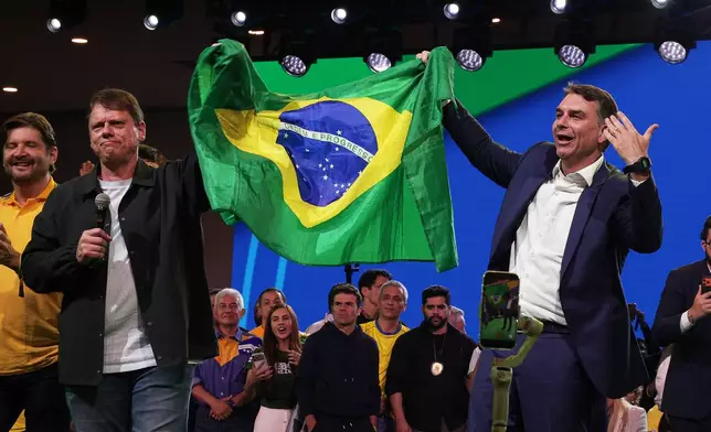 Brazilian Sen. Flavio Bolsonaro, right, and Sao Paulo Gov. Tarcisio de Freitas hold up their country's national flag during the Liberal Party convention where Bolsonaro was confirmed as the party's presidential candidate in Sao Paulo, Saturday, July 25, 2026. (AP Photo/Ettore Chiereguini)