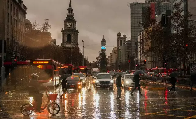 People cross Alameda Bernardo O'Higgins Avenue during a rainstorm in Santiago, Chile, early Monday, July 20, 2026. (AP Photo/Esteban Felix)x)