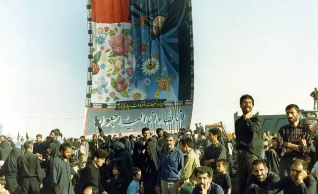 FILE - Mourners crowd around a huge banner with a picture of the late Ayatollah Khomeini at a cemetery in Beheshte e Zahra, some 70 kms from Tehran, Iran, June 11, 1989. (AP Photo/Heribert Proepper, File)