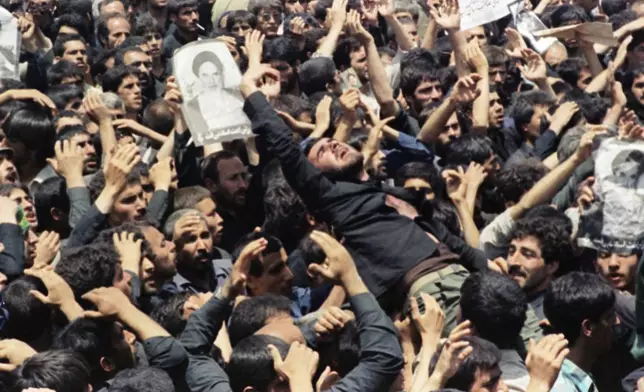 FILE - An Iranian mourner goes into a frenzy just after the body of the Ayatollah Khomeini was removed from Beheshte Zahra Cemetery in Tehran, June 6, 1989. The burial was delayed when thousands of mourners crowded the imam's body in an effort to touch their leader. (AP Photo/Greg English, File)