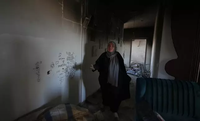 Ihsan Yaghi gestures inside her fire-damaged home, showing what she says, is graffiti left by Israeli forces, following a military operation, in Zawtar al-Gharbieh, Lebanon, Tuesday, July 28, 2026. (AP Photo/Hassan Ammar)