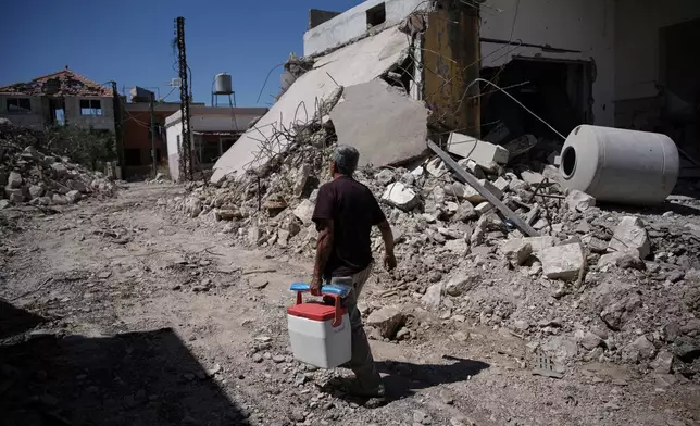 Mohammed Sobeih returns to his home, destroyed during the Israeli military operation, carrying a cooler in Zawtar al-Gharbieh, Lebanon, Tuesday, July 28, 2026. (AP Photo/Hassan Ammar)