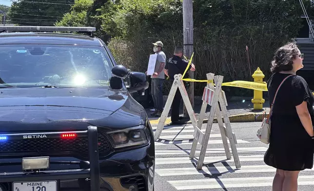 People stand near the scene as police block a road after a shooting involving U.S. Immigration and Customs Enforcement, in Biddeford, Maine, Monday, July 13, 2026. (AP Photo/Patrick Whittle)