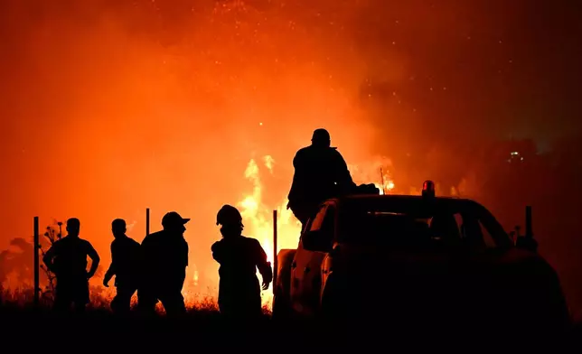 Firefighters and others are silhouetted in front of a wildfire on the outskirts of the northern city of Thessaloniki, Greece, Saturday, July 4, 2026. (AP Photo/Giannis Papanikos)