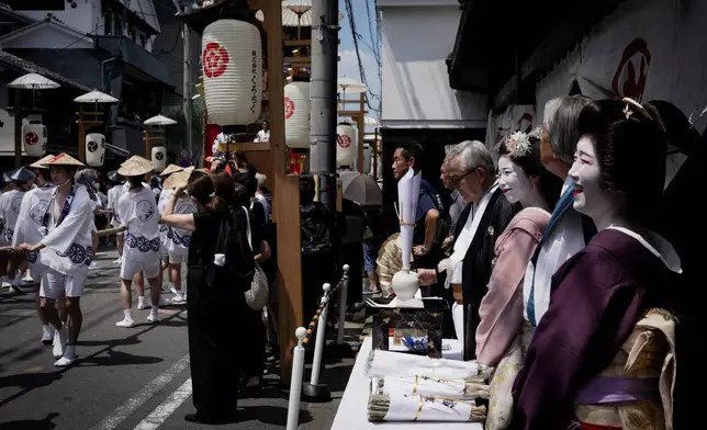 A geiko, a regional word for geisha, and a maiko watch festivalgoers pass by during one of the main parades of Shinto's Gion Matsuri festival in Kyoto, western Japan, Friday, July 17, 2026. (AP Photo/Fred Mery)