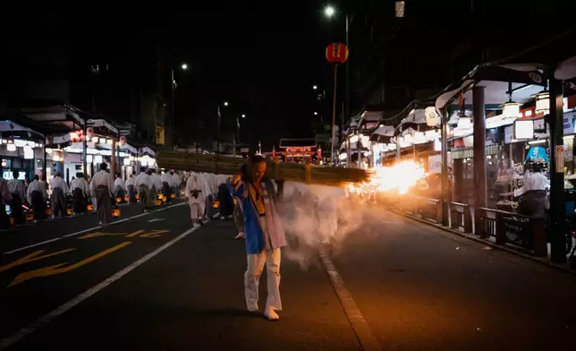 A festival participant carries a giant purification torch past tourists and local residents during the "Mikoshi Arai" purification ritual ahead of the Gion Matsuri festival in Kyoto, western Japan, Friday, July 10, 2026. (AP Photo/Fred Mery)