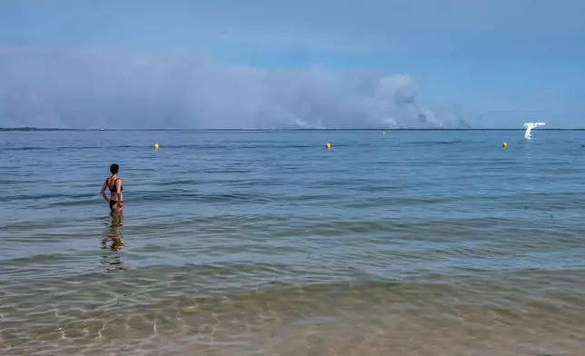 A woman watches smoke rising on the horizon from a beach in Arcachon as wildfires rage in western France, Friday, July 24, 2026. (AP Photo/Caroline Blumberg)