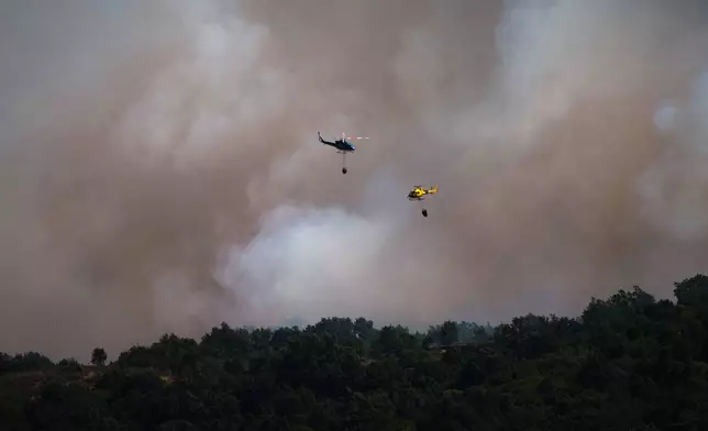 Firefighting helicopters drop water on the flames as a wildfire advances near Burgohondo, Ávila province, Spain, Friday, July 24, 2026. (AP Photo/Manu Fernandez)