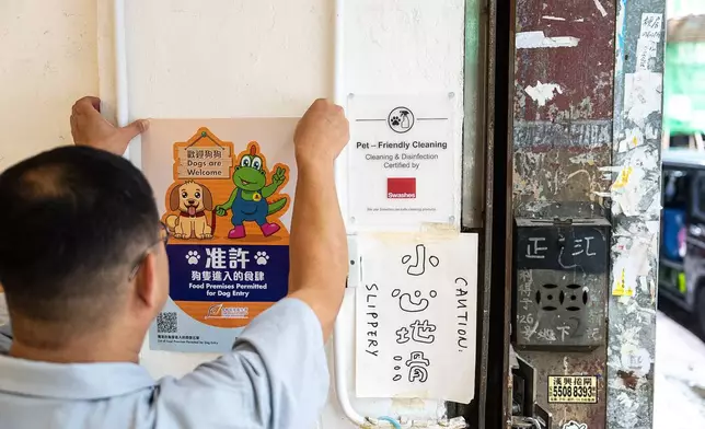 Wan Land Cafe owner Kelvin Chan sticks a poster inside the cafe indicates that dogs are legally permitted in dining premises in Hong Kong, Thursday, July 9, 2026. (AP Photo/Chan Long Hei)