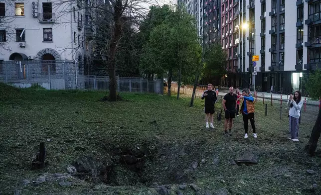 FILE - People stand by a crater from a Russian missile strike in the Lukianivka neighbourhood of Kyiv, Ukraine, May 24, 2026. (AP Photo/Evgeniy Maloletka)