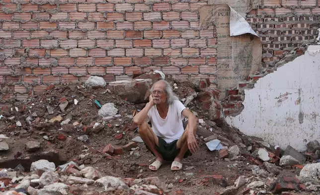A local resident sits on the ground of his demolished house, watching the demolition in his neighborhood to clear site for a new bridge crossing the Red river in Hanoi, Vietnam, Friday, June 5, 2026. (AP Photo/Hau Dinh)