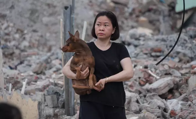 A woman carries her dog as she leaves her home that has been partially demolished to build a new ring road in Hanoi, Vietnam, Thursday, June 11, 2026. (AP Photo/Hau Dinh)