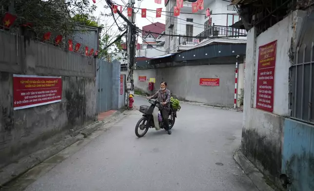 A woman rides a moped past banners put up by local residents to call for stopping a project that would displace the entire village by the Red river in Hanoi, Vietnam, Thursday, June 11, 2026. (AP Photo/Hau Dinh)