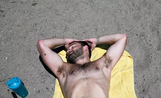Jack Scheck, of Minneapolis, lays in the sand after a run during an extreme heat warning, Monday, July 13, 2026, in Minneapolis. (AP Photo/Ellen Schmidt)