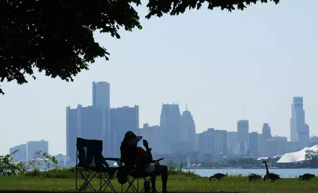 A woman sits in the shade to avoid the heat Monday, July 13, 2026, in Detroit. (AP Photo/Paul Sancya)