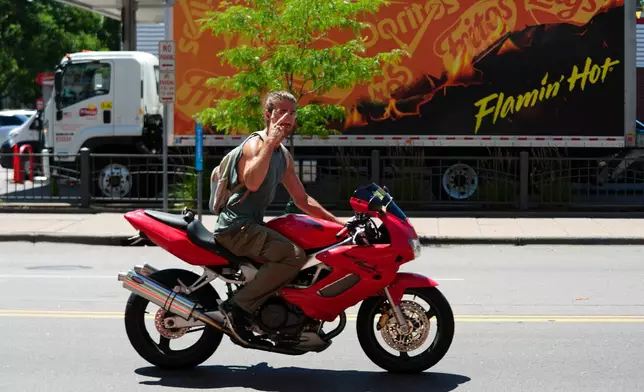 A motorist gestures while driving on West Lake Street during an extreme heat warning Monday, July 13, 2026, in Minneapolis. (AP Photo/Ellen Schmidt)