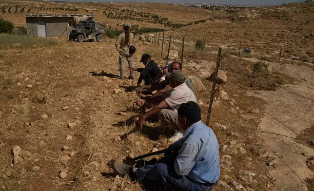 After Israeli soldiers told them to remain by the fence, Palestinians and an Israeli activist sit watching as settlers arrive in a vehicle after the settlers accused a local Palestinian resident of setting fire to a field, near the West Bank village of Susya in the Masafer Yatta region, Thursday, June 18, 2026. (AP Photo/Leo Correa)