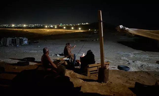 Palestinians sit next to a fire as they take part in a night watch to warn neighbors if Israeli settlers approach their community near the West Bank village of Susya, in the Masafer Yatta region, Thursday, June 18, 2026.. (AP Photo/Leo Correa)