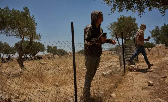 An Israeli settler steps into the courtyard of a home as another stands next to the fence, trespassing on Palestinian property on the outskirts of the West Bank town of Taybeh, Thursday, June 25, 2026. (AP Photo/Leo Correa)