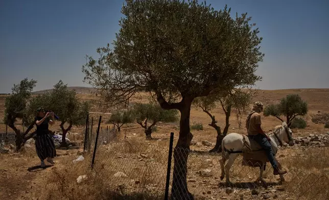 An Israeli activist records the presence of a settler as he moves with his donkey in front of a Palestinian house on the outskirts of the West Bank town of Taybeh, Thursday, June 25, 2026. (AP Photo/Leo Correa)