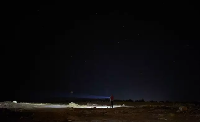 A Palestinian uses a flashlight as he takes part in a night watch to warn neighbors if Israeli settlers approach his community near the West Bank village of Susya, in the Masafer Yatta region, Thursday, June 18, 2026.. (AP Photo/Leo Correa)