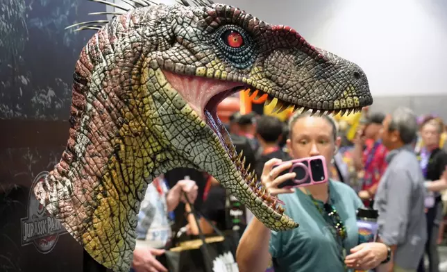 A Comic-Con attendee takes a cell phone picture of a bust of a male velociraptor from the film "Jurassic Park III" at the Elite Creature Collectibles booth during preview night at Comic-Con International on Wednesday, July 22, 2026, in San Diego. (AP Photo/Chris Pizzello)