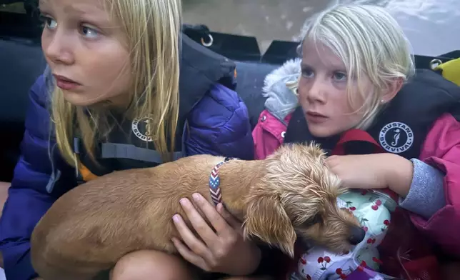 Ella and Grace Sanford and their dog Benjamin ride on a Texas Game Wardens rescue boat after being evacuated from their home after flooding in Uvalde, Texas, on Thursday, July 16, 2026. (Casy Sanford via AP)