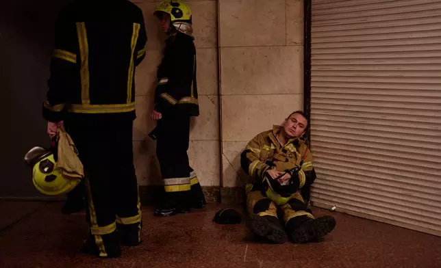 Firefighters shelter in a metro station following a siren alarm while they were trying to put out a fire at a city book market following a Russian missile attack in Kyiv, Ukraine early Sunday, Aug. 16, 2026. (AP Photo/Francisco Seco)