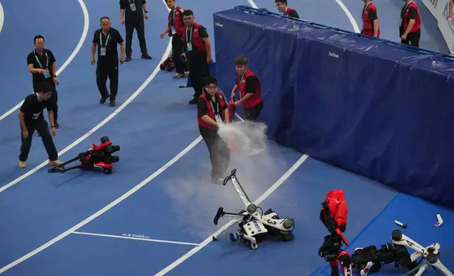 Official extinguish the fire to a Humanoid robot after hitting the barrier at the end of the 100m race during the World Humanoid Robot Games in Beijing, Tuesday, Aug. 25, 2026. (AP Photo/Achmad Ibrahim)