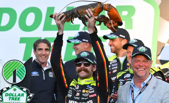 Ryan Blaney, center front, displays a lobster, a Victory Lane tradition at New Hampshire Motor Speedway, after winning a NASCAR Cup Series auto race, Sunday, Aug. 23, 2026, at the speedway in Loudon, N.H., as David McGrath, right, executive vice president and general manager of the speedway looks on. (AP Photo/Steven Senne)
