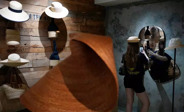 A Russian tourist tries on a hat and takes a selfie at a shop in Athens, Greece, Tuesday, Aug. 11, 2026. (AP Photo/Thanassis Stavrakis)