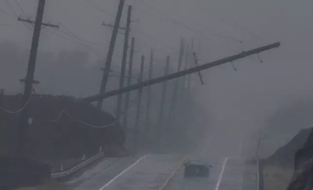 A vehicle drives near a downed utility pole dangling above Mamalahoa Highway during Hurricane Lala near Ocean View, Hawaii, Saturday, Aug. 15, 2026. (Stephen Lam/San Francisco Chronicle via AP)