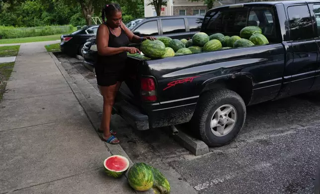 Rhonda Bracy cuts watermelons outside her home in Salisbury, Md., Saturday, Aug. 1, 2026. (AP Photo/Luis Andres Henao)