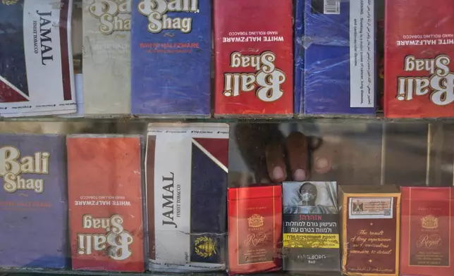 A vendor reaches for a pack of cigarettes at his kiosk in Deir al-Balah, central Gaza Strip, Friday, Aug 14, 2026. (AP Photo/Abdel Kareem Hana)