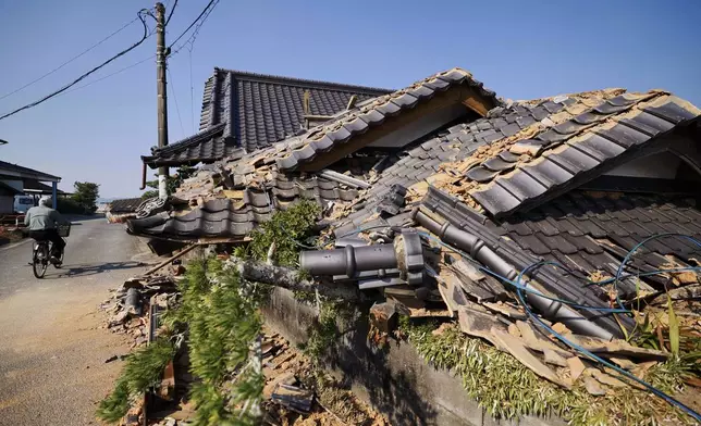 A person rides a bicycle past damaged buildings in Hikawa, southern Japan, Sunday, Aug. 2, 2026, following a July 28 earthquake. (Taichi Nagahisa/Kyodo News via AP)
