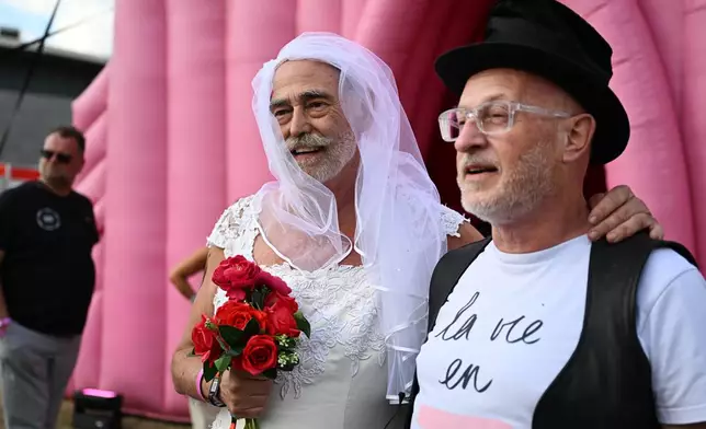 Newlyweds Jan Derksen-Wynn, left, and John Wijfjes pose for photos after tying the knot during a mass wedding ceremony in an inflatable chapel in Amsterdam, Netherlands, Thursday, Aug. 6, 2026, as part of Pride events celebrating 25 years since the Netherlands became the first country in the world to legalize same-sex marriage. (AP Photo/Mouneb Taim)