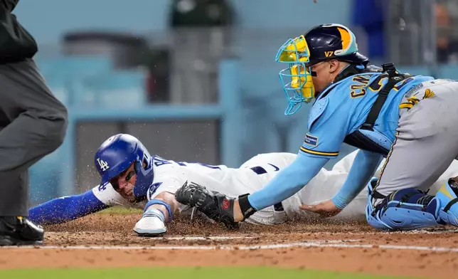 Los Angeles Dodgers' Miguel Rojas, left, scores on a single by Ben Rortvedt as Milwaukee Brewers catcher William Contreras tries to tag him without the ball after missing the throw during the fifth inning of a baseball game Thursday, Aug. 13, 2026, in Los Angeles. (AP Photo/Mark J. Terrill)