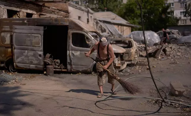 A local resident removes scattered debris next to destroyed vehicles the day after a Russian missile and drone attack in Kyiv, Friday, Aug. 21, 2026. (AP Photo/Francisco Seco)