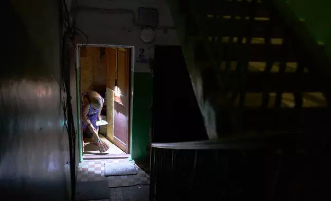 Larysa Polishchuk, 76, cleans the entrance of her apartment in a partially damaged residential building the day after a Russian missile and drone attack in Kyiv, Friday, Aug. 21, 2026. (AP Photo/Francisco Seco)