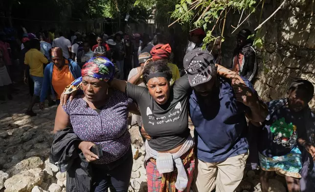 People watch as the bodies of their relatives who were killed in a gang attack are carried away by morgue workers in the Kenscoff neighborhood of Port-au-Prince, Haiti, Monday, Aug. 24, 2026. (AP Photo/Odelyn Joseph)