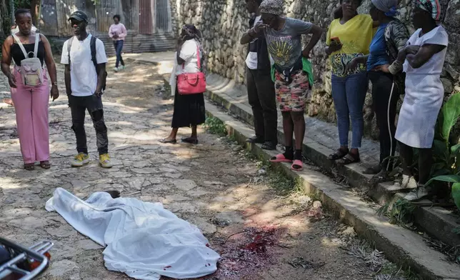 People look at the body of a person who was killed during a gang attack in the Kenscoff neighborhood of Port-au-Prince, Haiti, Monday, Aug. 24, 2026. (AP Photo/Odelyn Joseph)